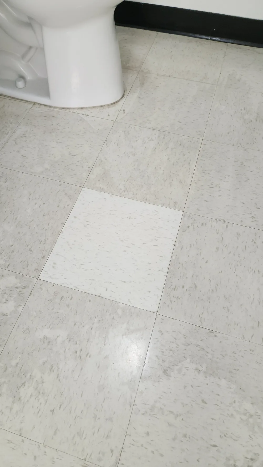 Real Total Cleaning Service VCT test spot — one freshly stripped and recoated bright tile in the middle of the surrounding dingy floor
